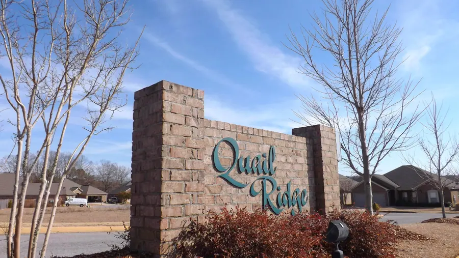 Brick Quail Ridge entrance monument with teal script lettering, crepe myrtles and brick homes behind it