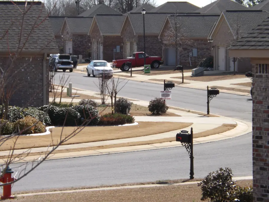 Curving street of brick homes with gabled roofs, mailboxes and young landscaping in Quail Ridge