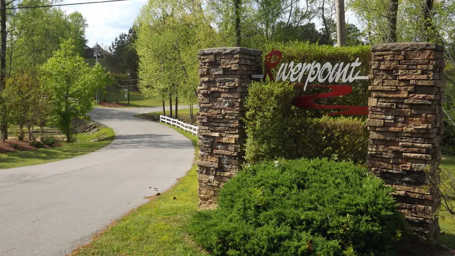 Stacked-stone entrance columns and the red Riverpoint sign beside a curving paved road and white fence